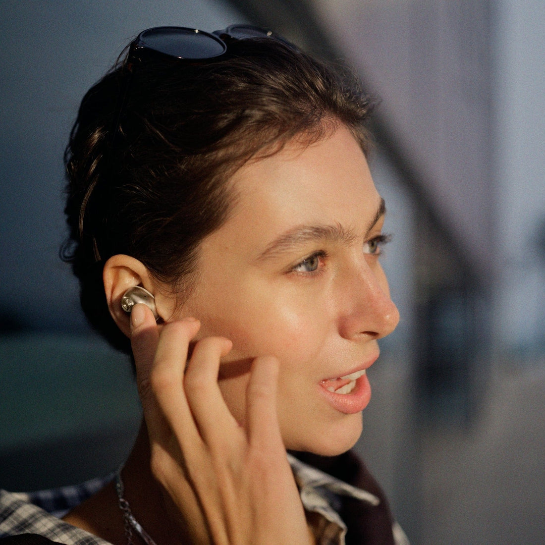 Person wearing a Sennheiser Momentum True Wireless 5 earbud, adjusting it in the ear in evening light