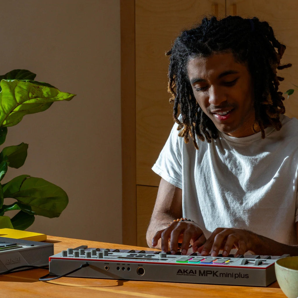 Akai Professional MPK Mini Plus II on a wooden desk with a producer playing